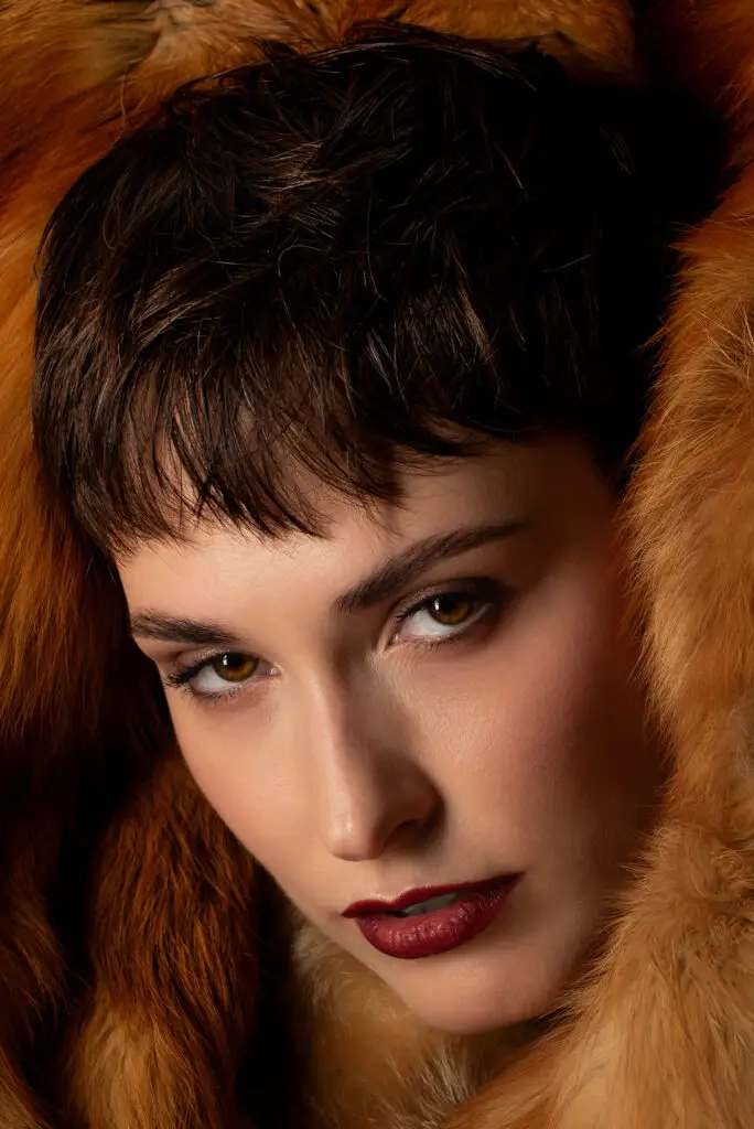 Retrato editorial de mujer con abrigo de piel ámbar y mirada pensativa, destacando el estilo sofisticado.