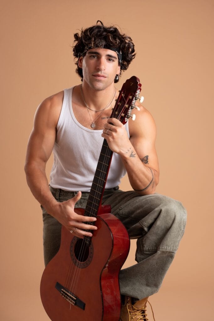 Retrato artístico de músico con guitarra y fondo beige en estudio fotográfico de Mallorca