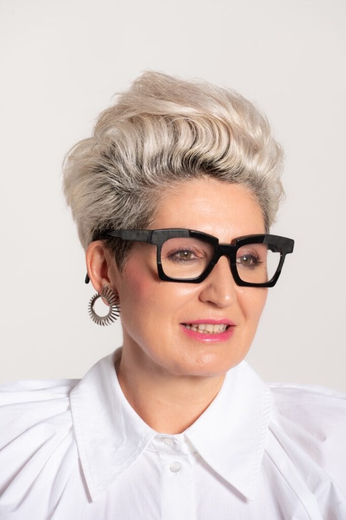 fotografia marca personal mallorca mujer gafas blanca elegante fotografia-de-marca-personal-mallorca Primer plano de mujer con gafas de pasta negra, pelo corto rubio y blusa blanca