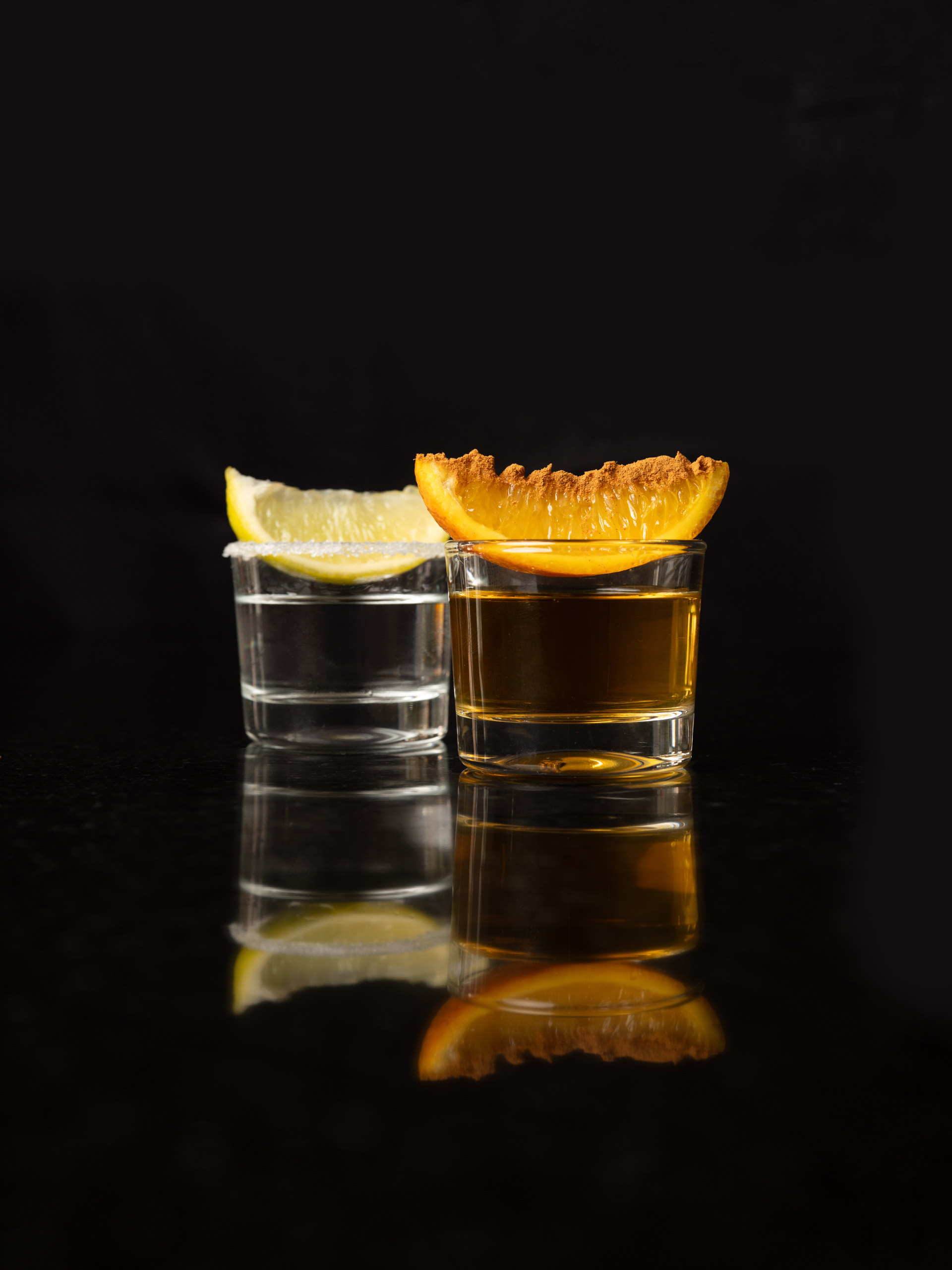 Chupitos de tequila con lima y naranja con canela sobre fondo negro, fotografía gastronómica en Mallorca por Flor Rajo