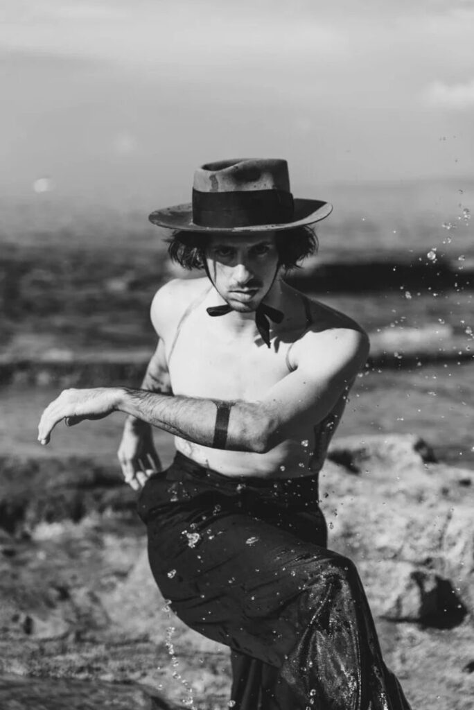 Artista con sombrero y falda en blanco y negro sobre las rocas junto al mar