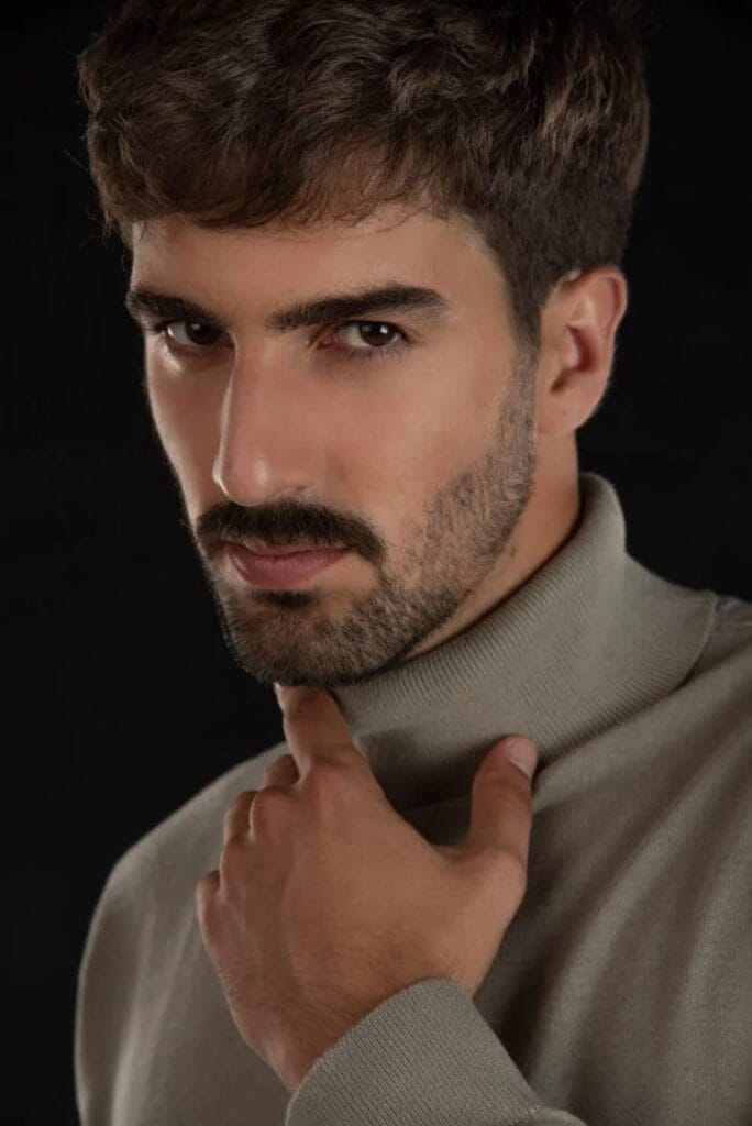 Retrato de hombre con barba y jersey de cuello alto sobre fondo negro